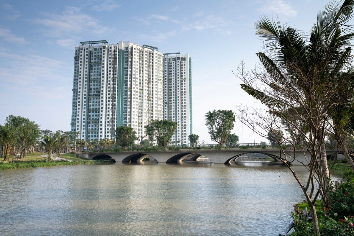 Two white-and-teal high-rise condo towers behind an arched bridge over a calm river lined with palm trees